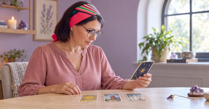 A beginner spiritual practitioner reflecting on tarot cards with a small crystal and pendulum in a quiet room.